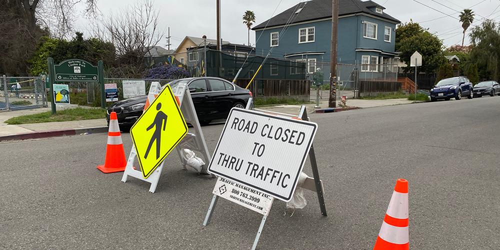 Orange cones, a pedestrian crosswalk sign and a "Road Closed to Thru Traffic" sign block traffic from entering the roadway on a Slow Street.