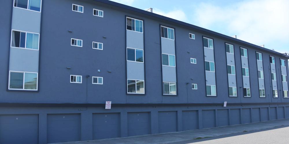 A large, soft-story apartment building with parking garage spaces on the first floor.