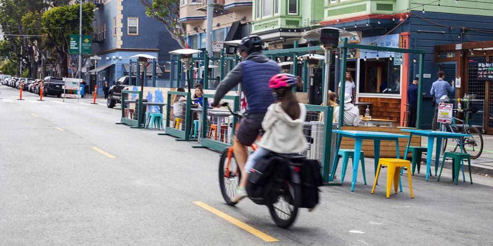 A cyclist rides next to streetside restaurant seating on a street that is closed to vehicles.