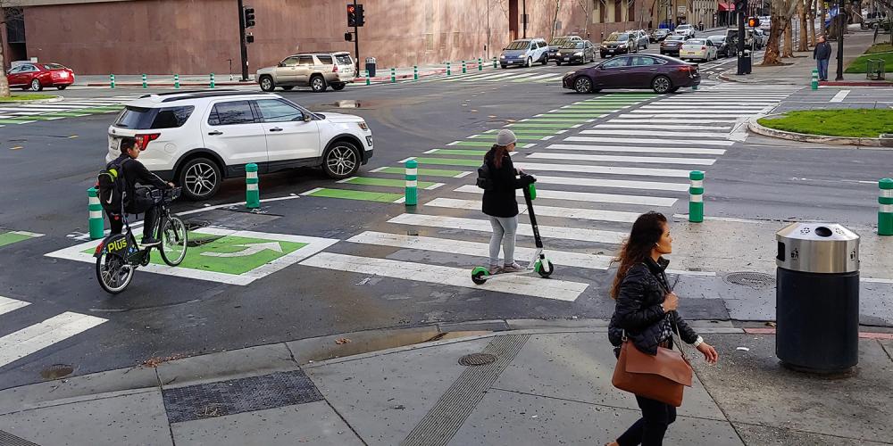Drivers, cyclists, pedestrians and scoooter users share a roadway intersection.