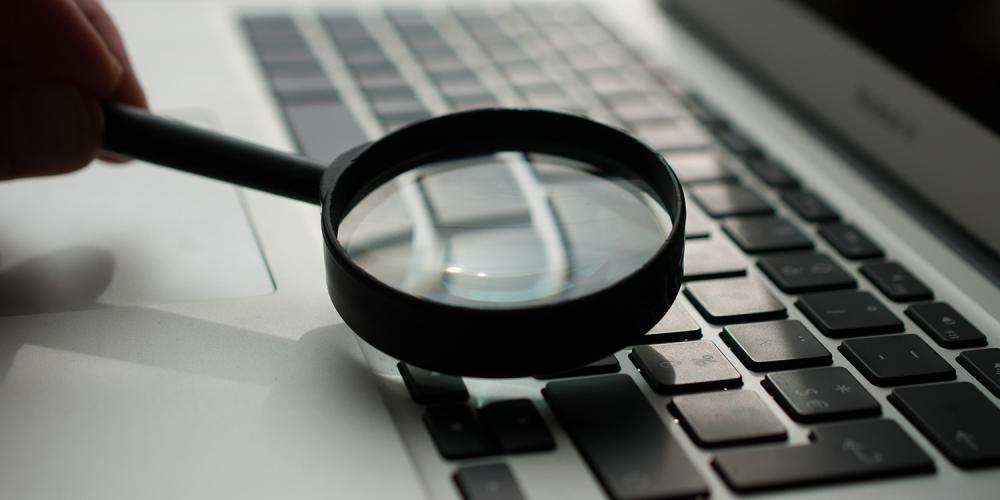 A magnifying glass resting on top of a laptop's keyboard.