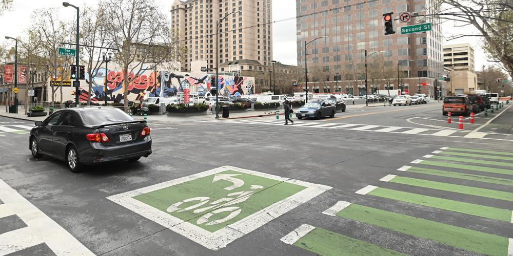 An intersection with a bike lane and green bike box on the pavement, using pavement parkings to create safter spaces for cyclists.