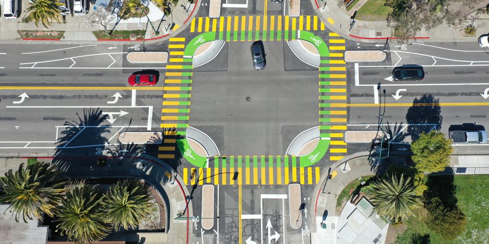 Aerial of an intersection with yellow pedestrian crosswalk markings and green bike lanes.