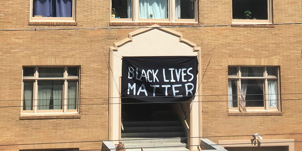A Black Lives Matter banner hanging on the front of a brick building.