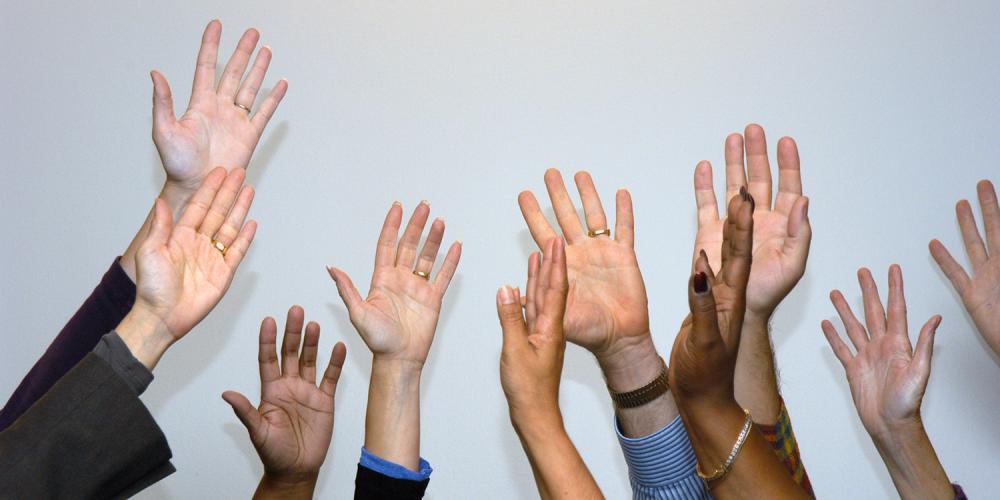 A diverse group of people with their hands raised.