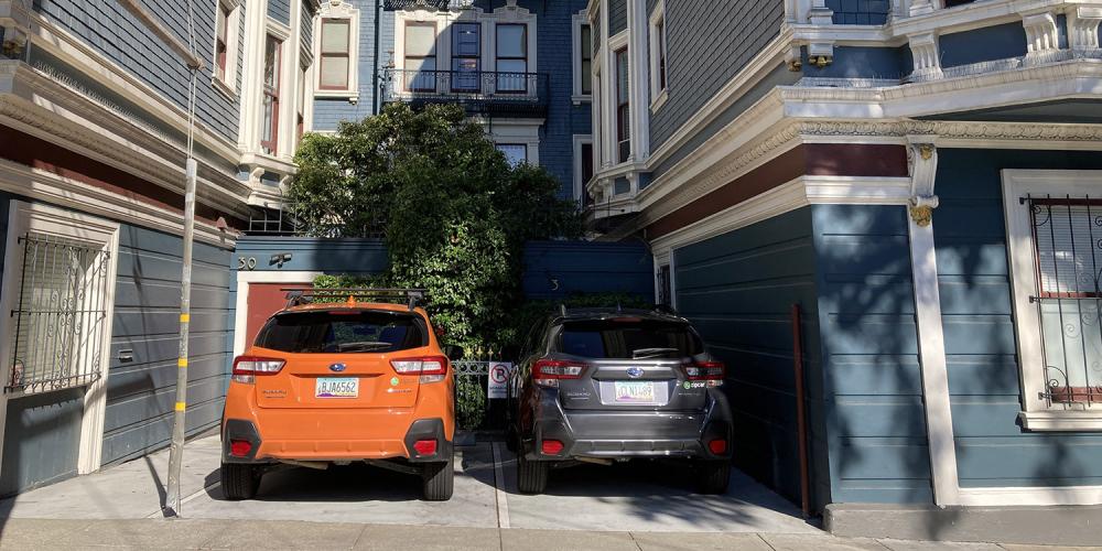 Two Zipcar car-sharing vehicles parked in a two-car lot at a residential building in San Francisco.