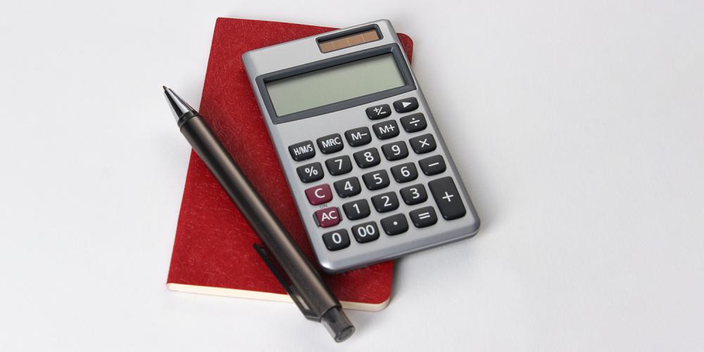 A calculator and a pen on top of a small, red notebook.