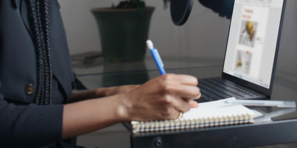 A person writing in a notebook while using a laptop computer.