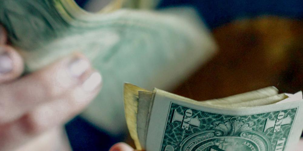 Close up of a person counting one-dollar bills.