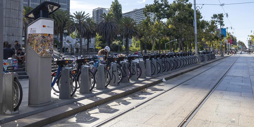 A person docks their bike at a bikeshare station alongside Muni train tracks in San Francisco.