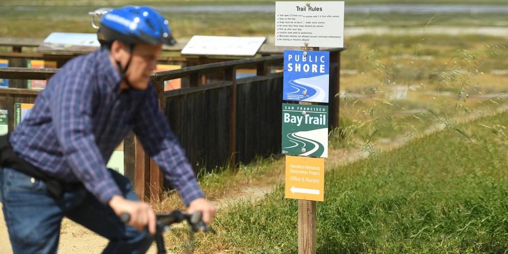 A cyclist rides past a Bay Trail sign.