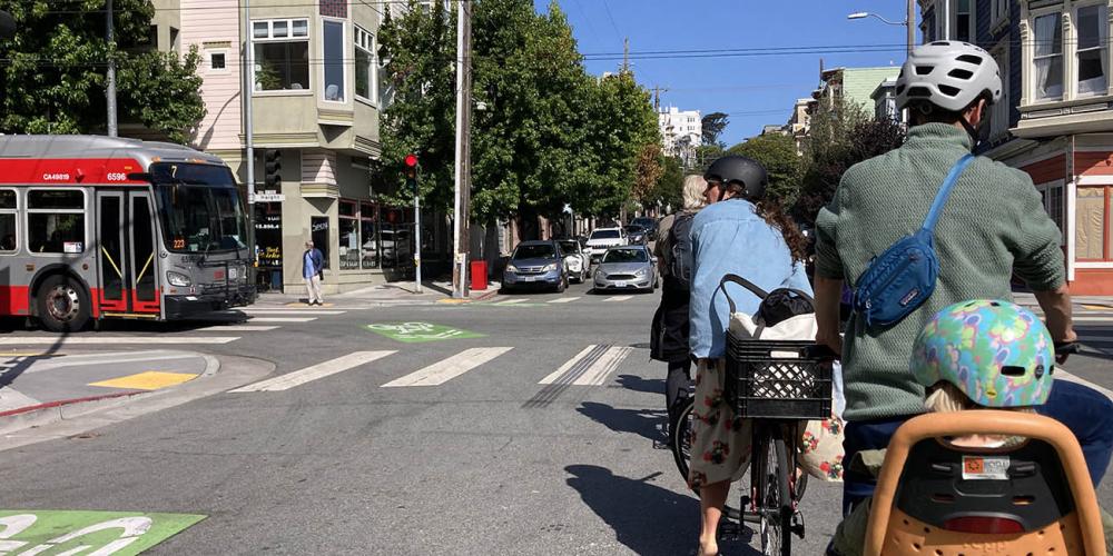 Cyclists wait for a Muni bus to pass by.