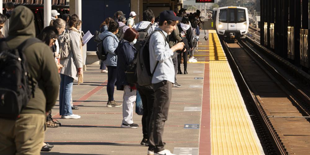 Passengers wait on the platform for a train at the Macarthur BART station