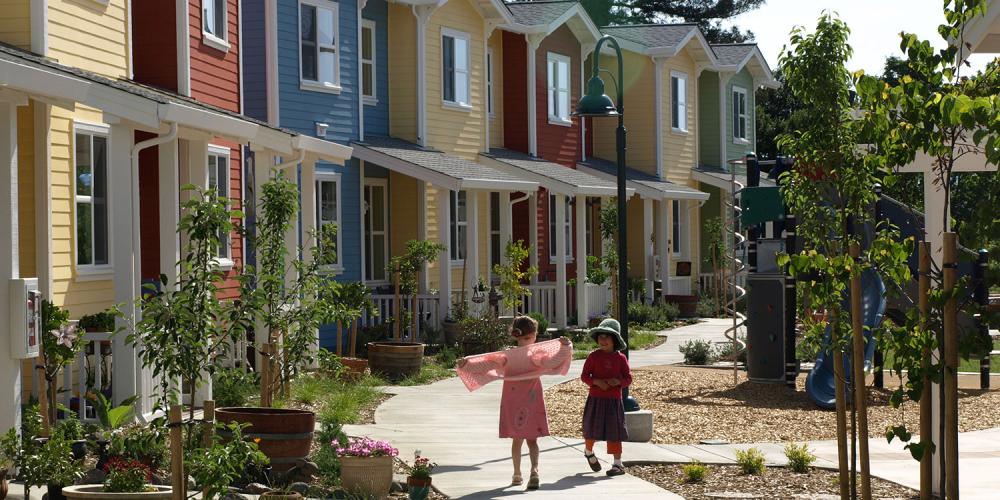 Row houses of bright colors, with two young children playing out front.