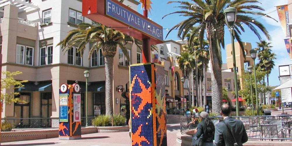 image is of 2 to 3 story buildings around a plaza with colorful artwork with people walking