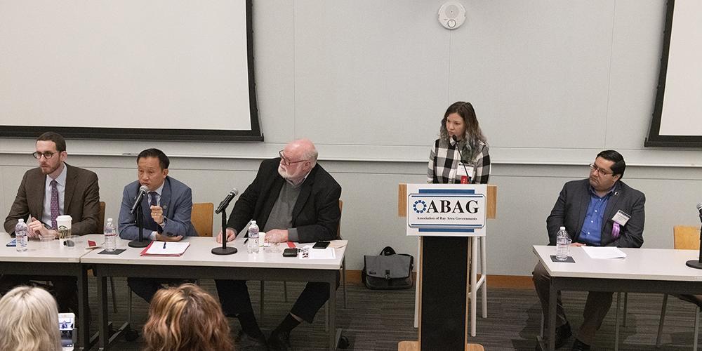 Speakers, men in suits on left, woman at podium with ABAG sign, man on right