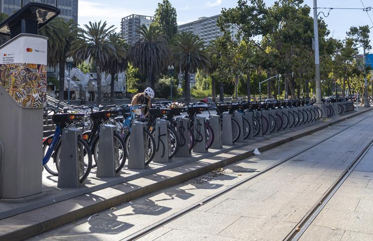A person docks their bike at a bikeshare station alongside Muni train tracks in San Francisco.