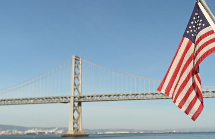 An American flag in front of the San Francisco-Oakland Bay Bridge.