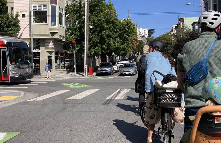 Cyclists wait for a Muni bus to pass by.