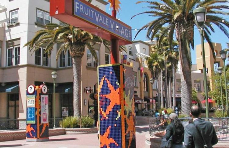 image is of 2 to 3 story buildings around a plaza with colorful artwork with people walking
