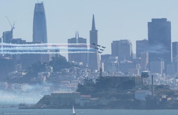 SF Skyline with blue angels flying by with red white and blue smoke. 